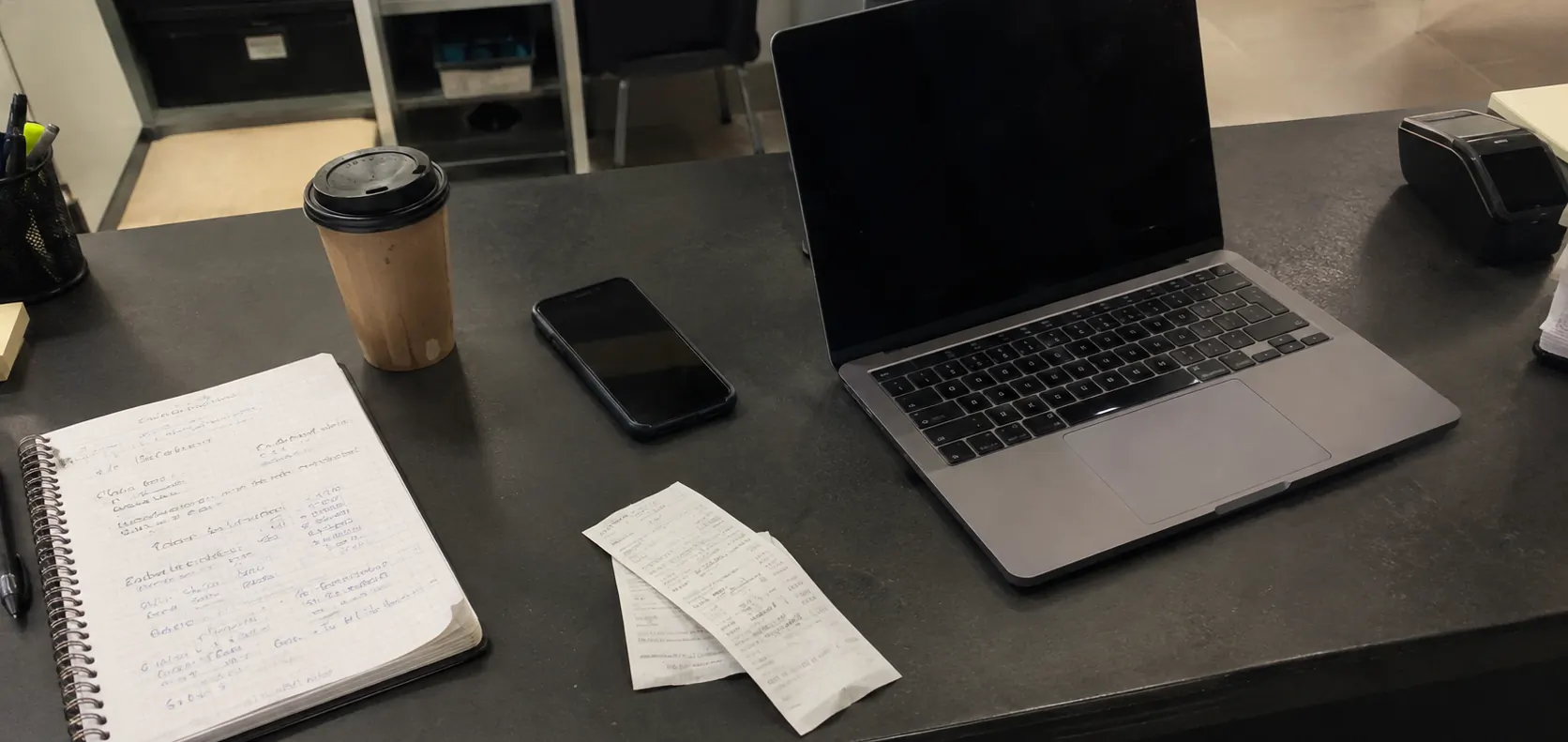 Mostrador de un negocio al cierre con un portátil, un móvil, una libreta con notas y dos tiques: lo que una IA lee de un negocio para recomendarlo